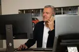 Adviseur Bert aan het bellen met mobiel aan z'n oor, achter bureau met computer